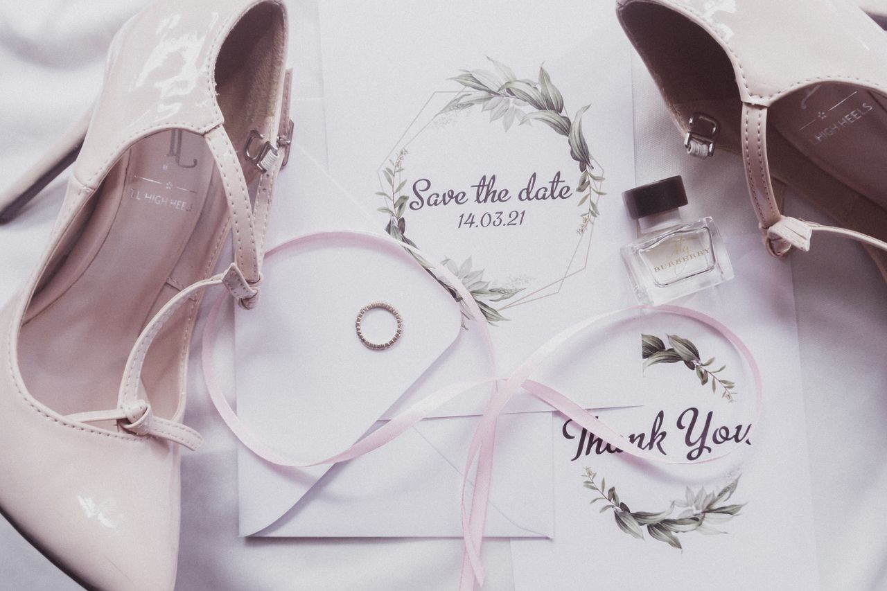 A stylish flat lay of wedding essentials, featuring heels, perfume, and invitations.